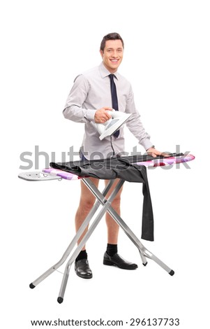 Full length portrait of a young man ironing his pants and looking at the camera isolated on white background