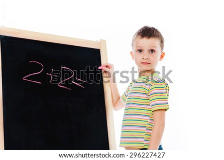 Nice boy trying answer simple math question; preschooler child writing basic math equation on a chalkboard; preschooler kid staying nearby chalkboard with a peace of chalk