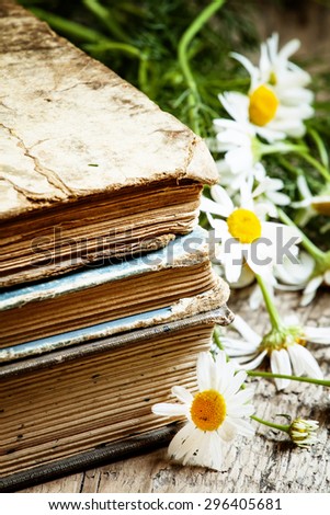Old books, bouquet of field daisies on a wooden background in vintage style, selective focus
