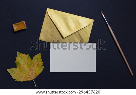 Autumn leaf on black background with card invitation and golden envelope
