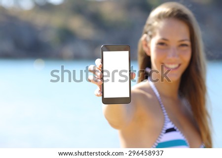 Sunbather woman wearing bikini showing blank phone screen on the beach in summer vacations