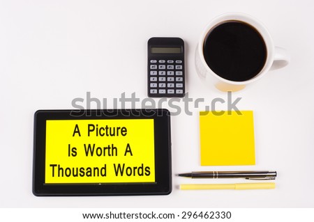 Business Term / Business Phrase on Tablet PC with a cup of coffee, Pens, Calculator, and yellow note pad on a White BG - Black Word(s) on a yellow background - A Picture Is Worth A Thousand Words