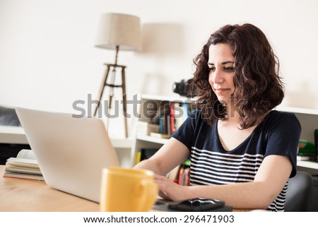 Happy girl using her laptop at home with yellow tea cup.