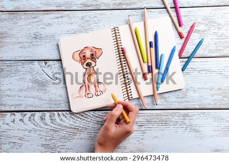 Female hand drawing dog in notebook on wooden table background