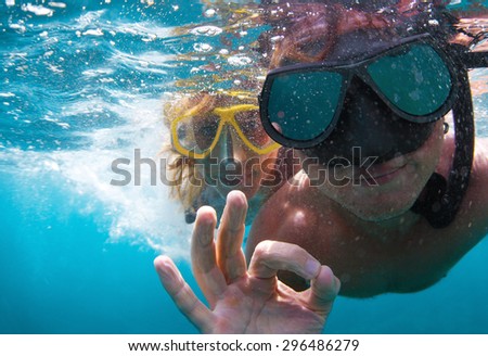 Young couple having fun underwater and showing ok sign