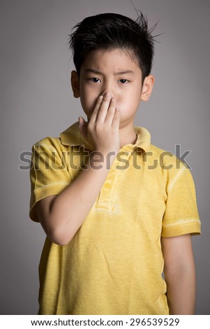 Young asian boy with both hands closing mouth on gray background