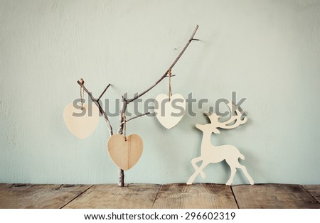 hanging wooden hearts over and wooden rain deer decoration over wooden background. retro filtered image
