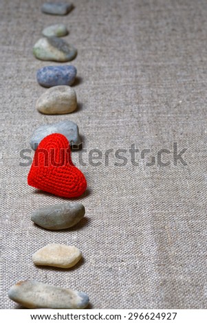Red heart in vertical row of stones on textile background. Shallow focus on heart.
