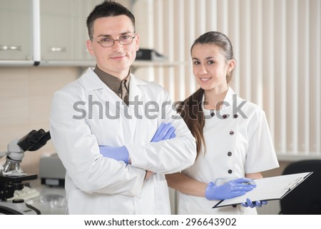young doctor and assistant standing and smiling in lab