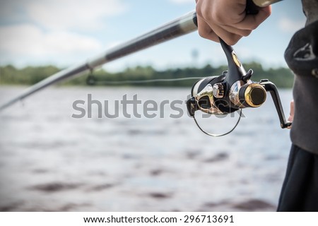 hand holding a fishing rod with reel. Focus on Fishing Reels  Royalty-Free Stock Photo #296713691