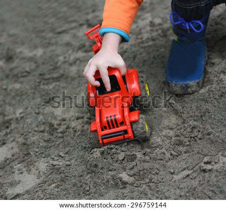the part of the image of a small child wearing rubber boots, which sits in the wet sand and plays with red toy construction machine.