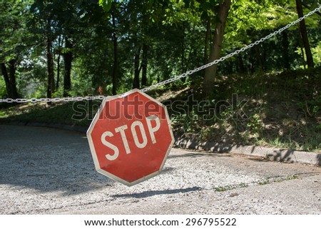 Stop sign at park.Hanging on chains. In the background is forest. It is the area that no cars are allowed.
