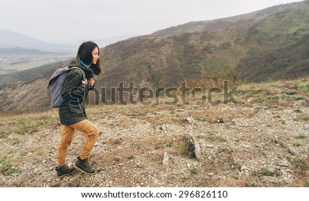 Hiker girl with backpack goes up in the mountain at cloudy weather