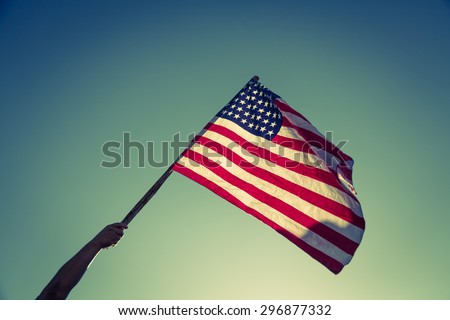 American flag with stars and stripes hold with hands against blue sky ( Filtered image processed vintage effect. ) Royalty-Free Stock Photo #296877332