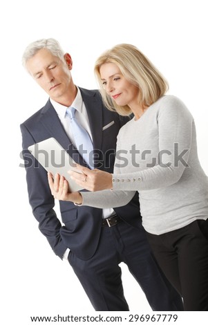 Portrait of middle age businesswoman standing against white background while holding digital tablet in her hands. Senior businessman standing next to her and working together.