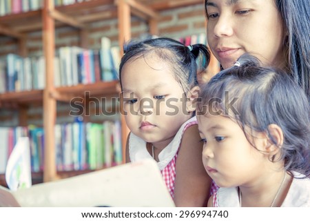 Mother and little daughter reading book together in library,vintage color filter