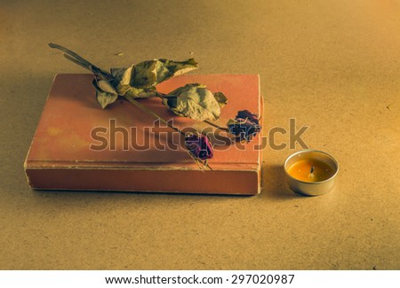 Vintage style. Lonely time an old book and wither rose near candle on wood background .Dark tone.