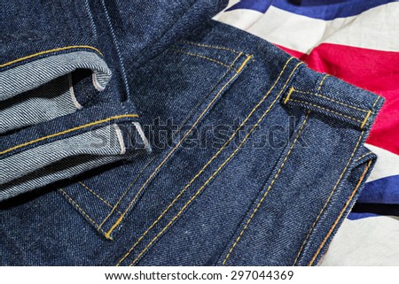 Blue Jeans Denim, 100% Cotton Un sanforized Denim Red Selvage Jeans on Plaid Shirt background, selective focus (detailed close-up shot) Royalty-Free Stock Photo #297044369