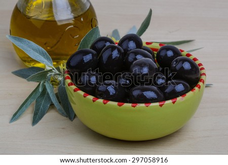 Black olives with leaves and oil on the wood background