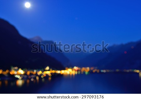City at night. Blurred photo.  Moon over silhouettes of mountains.