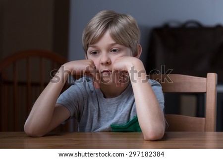 Picture of dissatisfied small blonde kid sitting at table