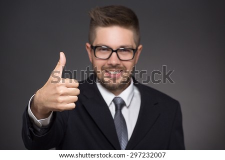 Happy businessman obtaining promotion. Short-haired bearded man in business suit showing okay sign and smiling on dark grey.