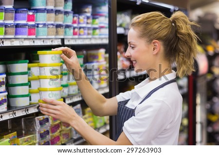 Smiling blonde worker taking a products in shelf in supermarket