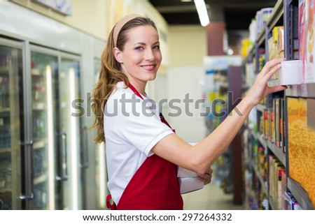 Happy pretty woman putting product on shelf at supermarket