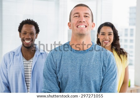 Smiling man in front of his colleagues looking at camera in the office