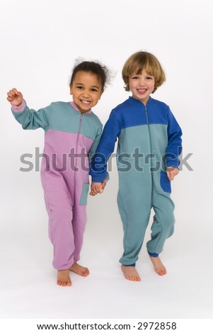 A beautiful mixed race little girl and a cute blond boy dressed in sleep suits holding hands, laughing and having fun together