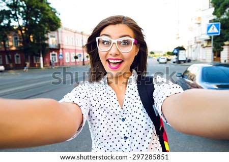 Young smiling teen happy woman making selfie on the street, ling hairs, bright make up and cute clear glasses, traveling alone, having fun, positive mood, joy, vacation, surprised emotions.