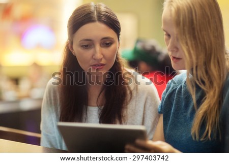 Serious blonde and brunette women talk in the restaurant watching something on the tablet