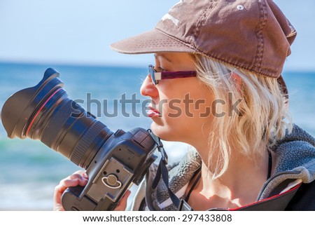 Woman professional photographer taking pictures on a beach, freehand. Sea landscape background.