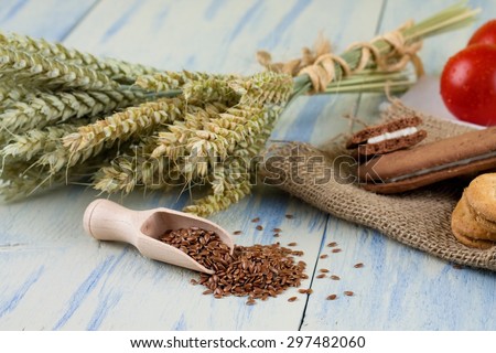 Horizontal photo of wooden spoon full of linseeds on white blue wooden board. Bonded grain ears and cereal biscuits on jute cloth are in background.