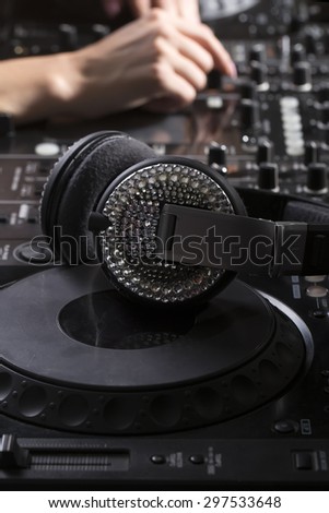 Musical clubbing professional equipment of black dj mixer console and glamour headphones with sparkles and female hand on background closeup, vertical picture