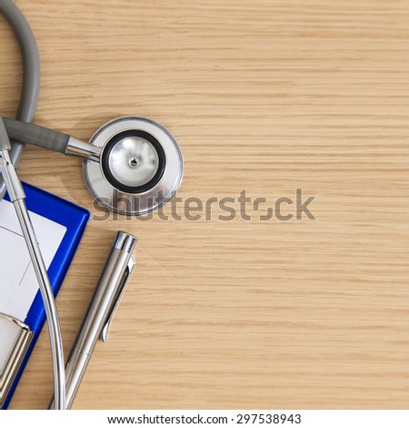 Stethoscope with medical clipboard, syringe, a pen and mobile phone on wooden table background