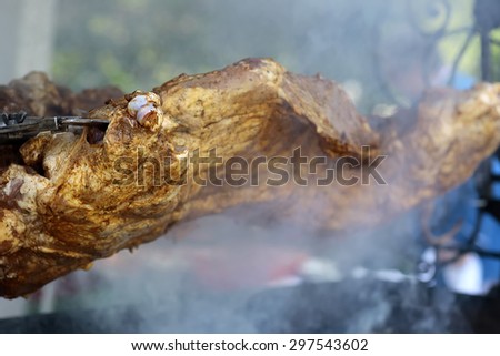 Large piece of fresh hot juicy tasty meat roasted on spit grille in smoke outdoor closeup, horizontal picture