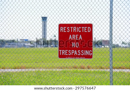 A RESTRICTED AREA NO TRESPASSING sign on a fence at an airport with the air traffic control tower in the background Royalty-Free Stock Photo #297576647