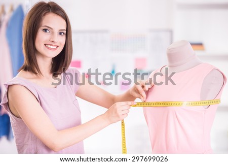 Confident woman measuring pink dress, looking at camera and smiling.