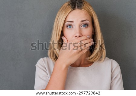 Shocking news. Surprised mature woman covering mouth with hand and staring at camera while standing against grey background Royalty-Free Stock Photo #297729842