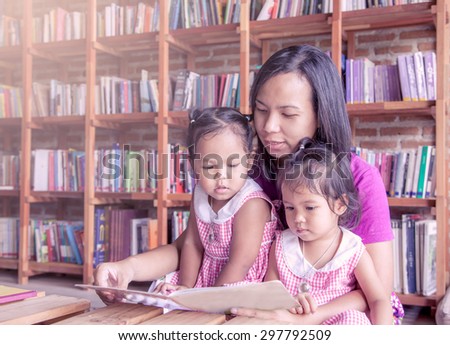 Mother and little daughter reading book together in library,soft color filter