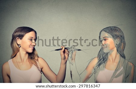 Create yourself, your future destiny, image, career concept. Attractive young woman drawing a picture, sketch of herself on grey wall background. Human face expressions, determination, creativity