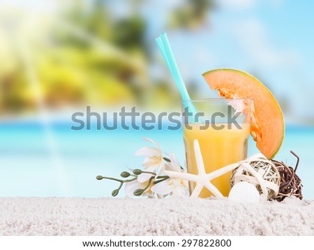Fresh orange juice on sand with blue sky background, summer concept
