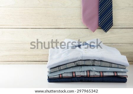 Stack of men shirts and tie hanging with white wooden background
