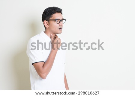 Portrait of Indian guy sore throat, hand on neck clearing throat. Asian man standing on plain background with shadow and copy space. Handsome male model. Royalty-Free Stock Photo #298010627