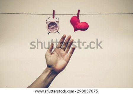 hands fighting to reach a clock and a red heart