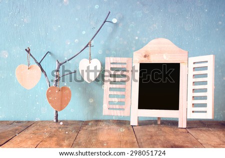 decorative chalkboard frame and wooden hanging hearts over wooden table. ready for text or mockup. retro filtered image with glitter overlay 