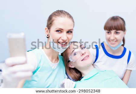 Young beautiful medical doctors dentist hygienist orthodontist and her assistant making selfie on their phone with happy patient smiling after successful treatment