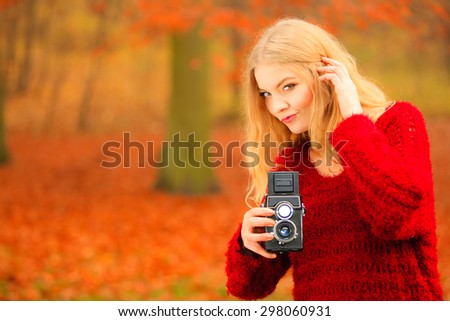 Fashionable blonde girl young woman female photographer walking in autumn park, taking photo picture with old vintage camera, orange leaves background