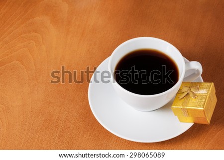 White coffee cup and gold gift box with bow on wooden background